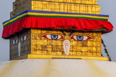 Le soleil couchant renforce la teinte dorée, alors qu'une faible brise soulève les étoffes colorées des cinq couleurs sacrées. Selon l'école Nyingma, bleu : l'espace, la voûte céleste (akasha) ; blanc : l'air, le vent, les nuages (vayu) ; rouge : le feu (agni) ; vert : l'eau (jala) ; jaune (ou orange) : la terre (prithvi).
Les yeux apaisés du Bouddha expriment simplement la connaissance ; leur regard porte dans les quatre directions : c'est l'omniscience de l'Éveillé, qui voit tout.
Et ce que l'on prend pour un nez n'en est pas un : c'est le chiffre 1 népalais, symbole de "l'unique", la voie unique vers l'illumination, celle de l'enseignement du Bouddha.
Enfin, le troisième œil, masqué par les banderoles, figure la sagesse.