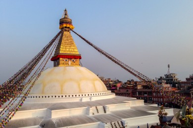 Vu d'en haut, Boudhanath dessine un immense mandala, image de l'univers bouddhiste : le dôme blanc, les drapeaux qui rayonnent, et tout autour le fourmillement du quartier tibétain. C'est l'heure où les pèlerins affluent pour la kora du soir et allument les lampes à beurre. Chaque étage du stupa figure d'ailleurs un élément, du plus terrestre au plus céleste : la base carrée, la terre ; le dôme, l'eau ; la flèche aux treize anneaux, le feu ; le parasol, l'air ; et le joyau qui le couronne, l'espace.